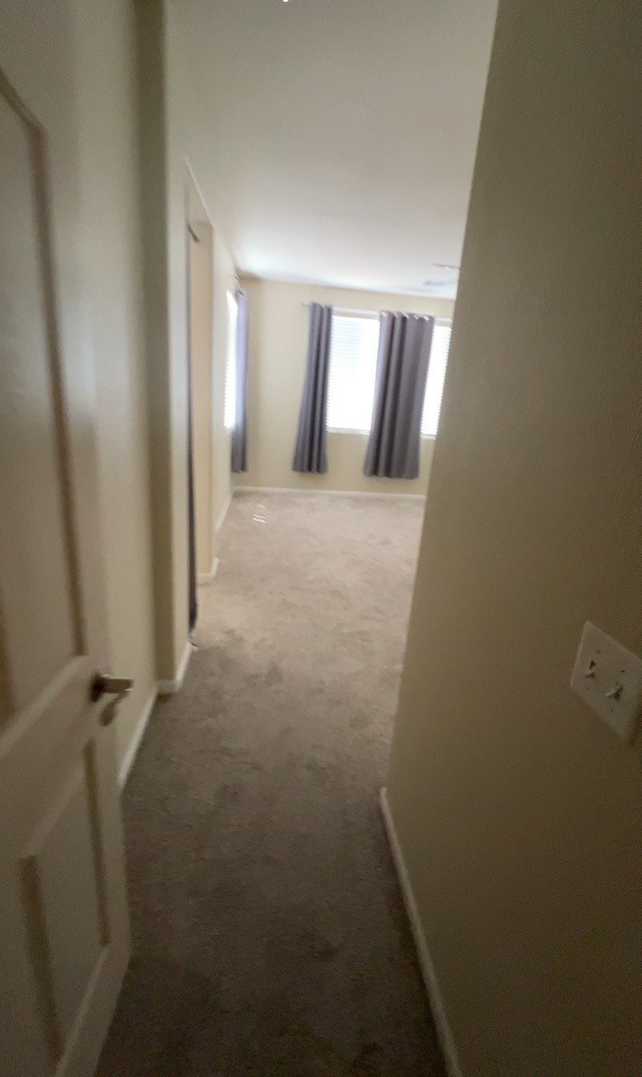 a hallway with a carpeted floor and a window with curtains