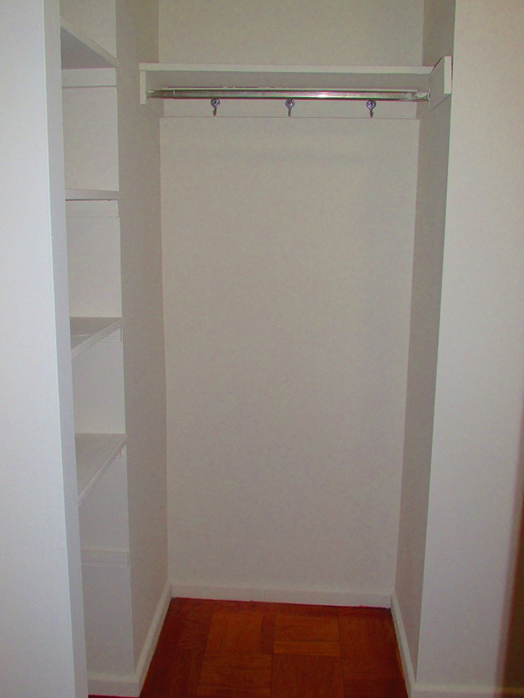 a closet with a white wall and shelves and a white closet door