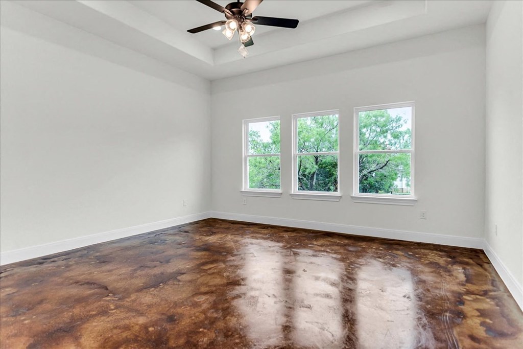 an empty living room with a ceiling fan and three windows