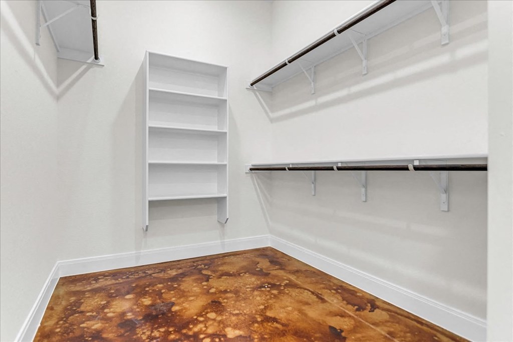 a walk in closet with white walls and shelves and a brown floor