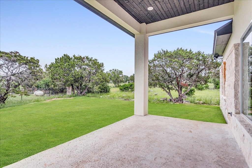 a covered patio with a lawn and trees in the background