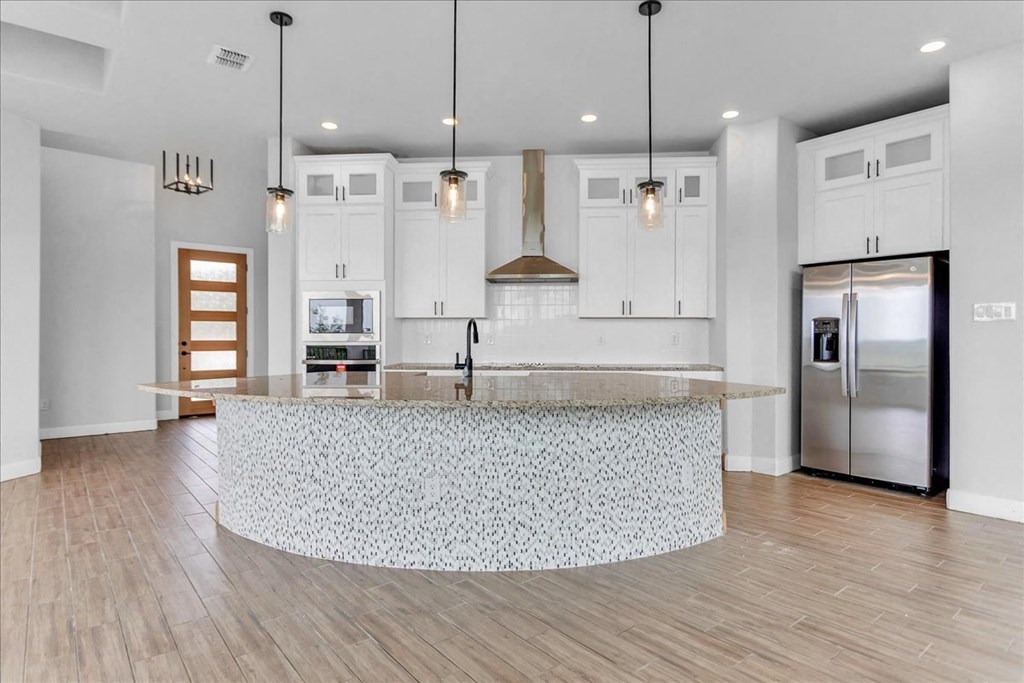 a white kitchen with a large island and a stainless steel refrigerator