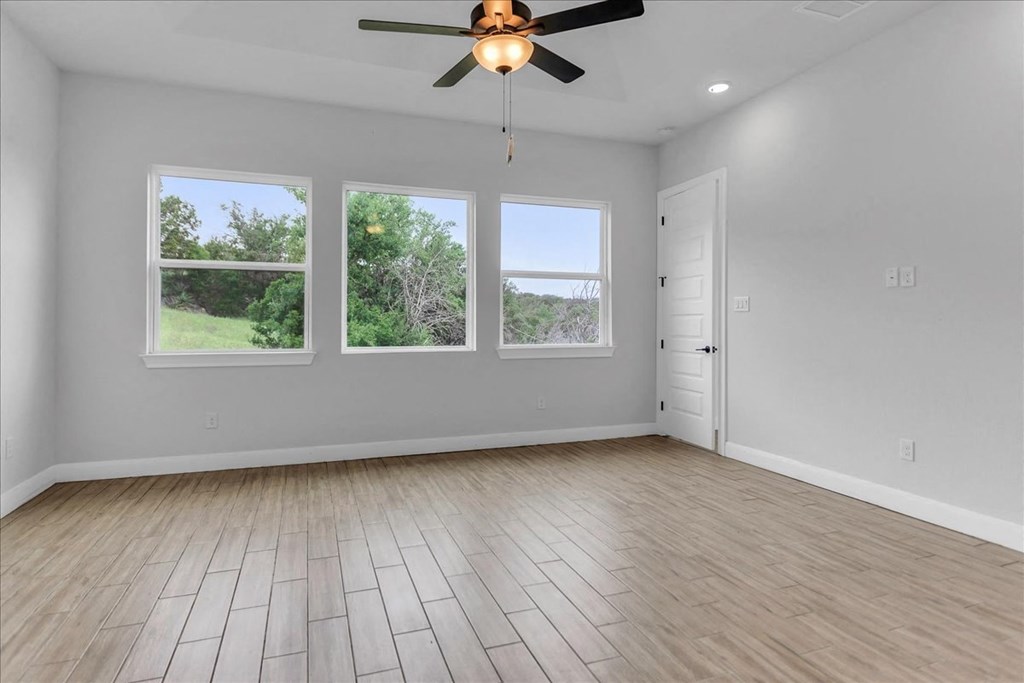 an empty living room with a ceiling fan and three windows