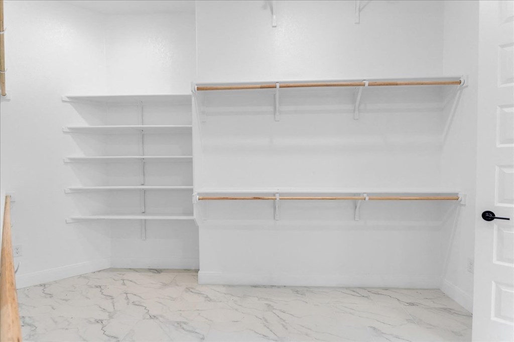 a walk in closet with white walls and shelves and a white closet door