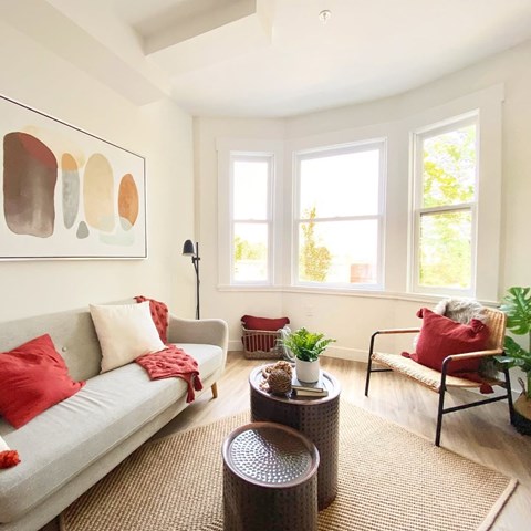 A living room with a grey couch, red pillows, and a painting on the wall.