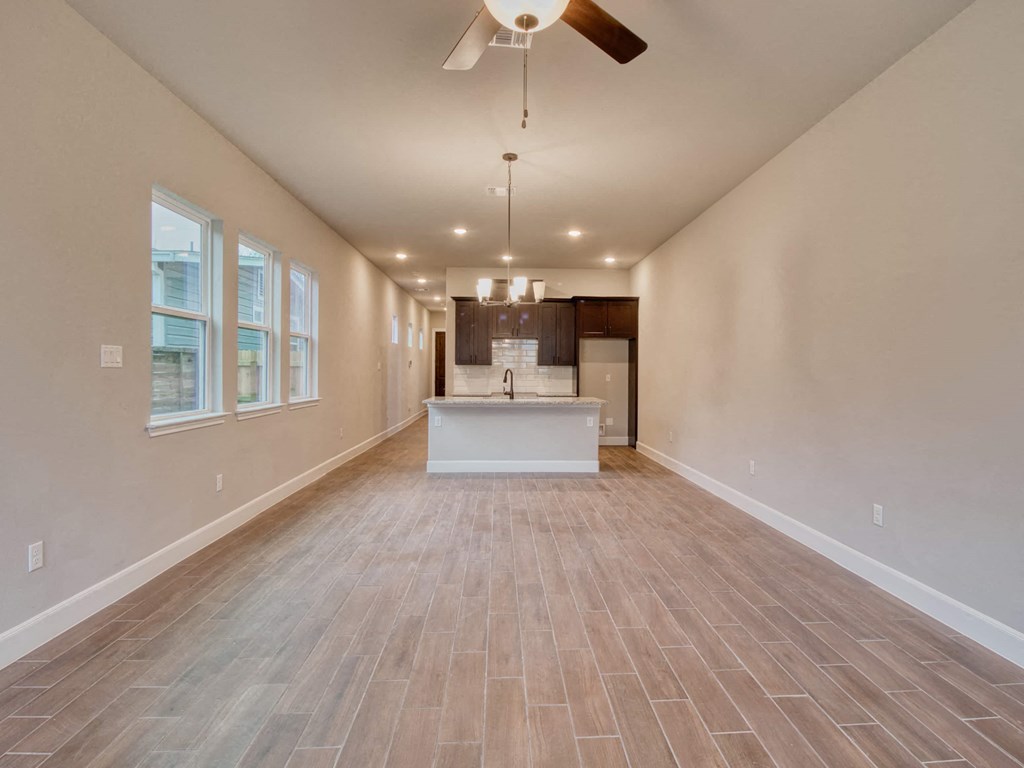 an empty living room with a kitchen and a ceiling fan