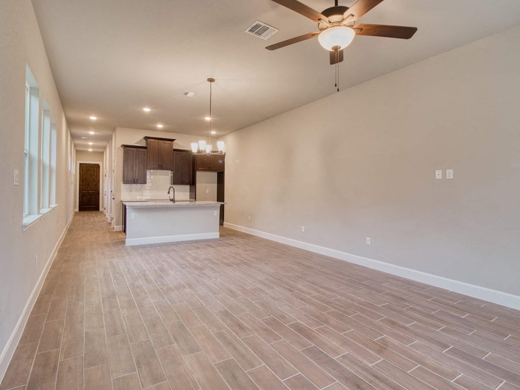 an empty living room with a kitchen and a ceiling fan