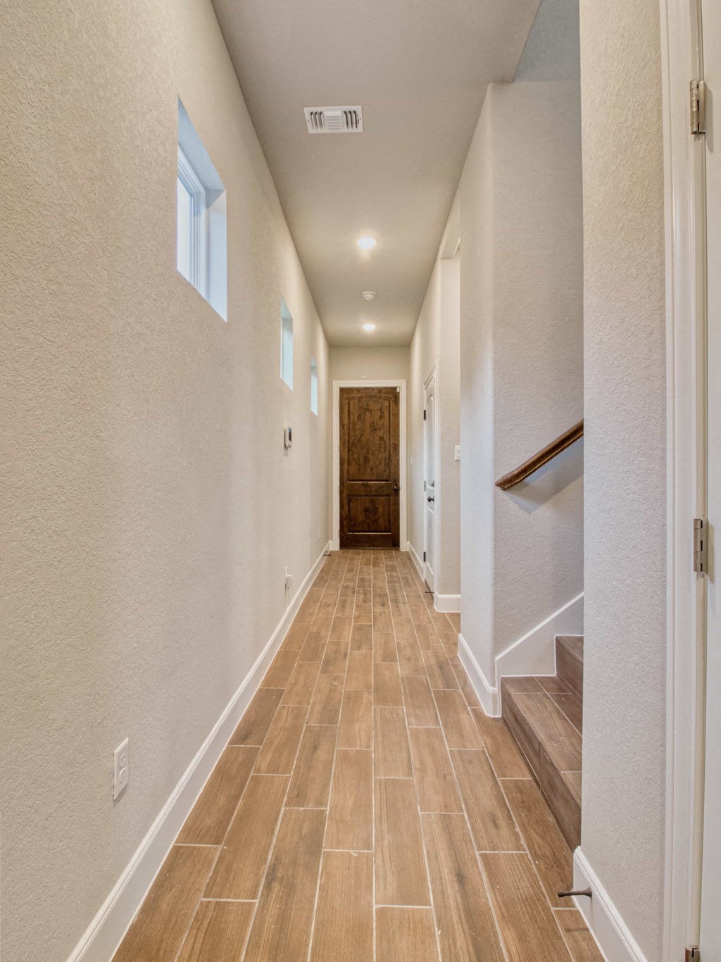 a long hallway with tile floors and white walls and a staircase