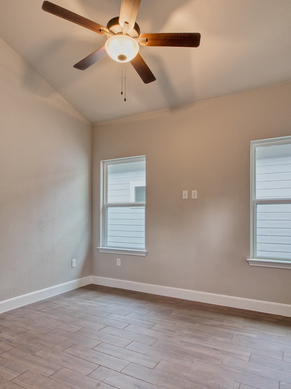 an empty living room with a ceiling fan and two windows