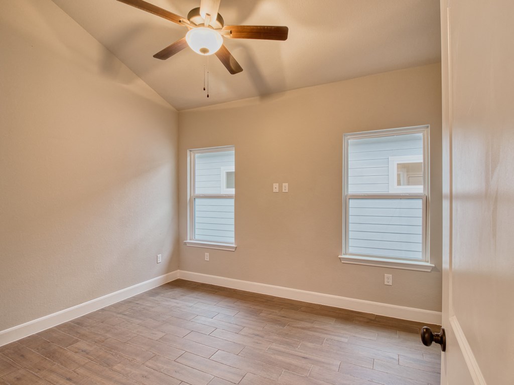an empty living room with a ceiling fan and windows
