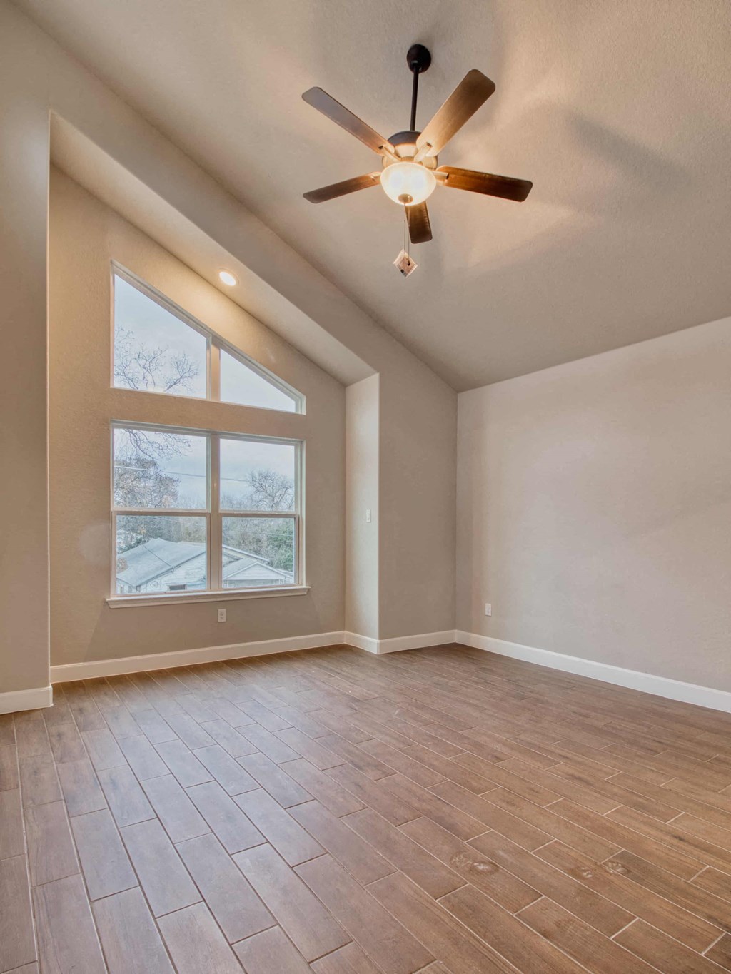 an empty living room with a large window and a ceiling fan
