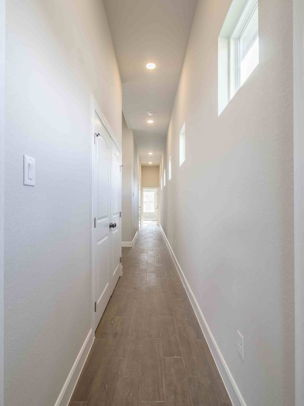 a long hallway with white walls and white doors and a window