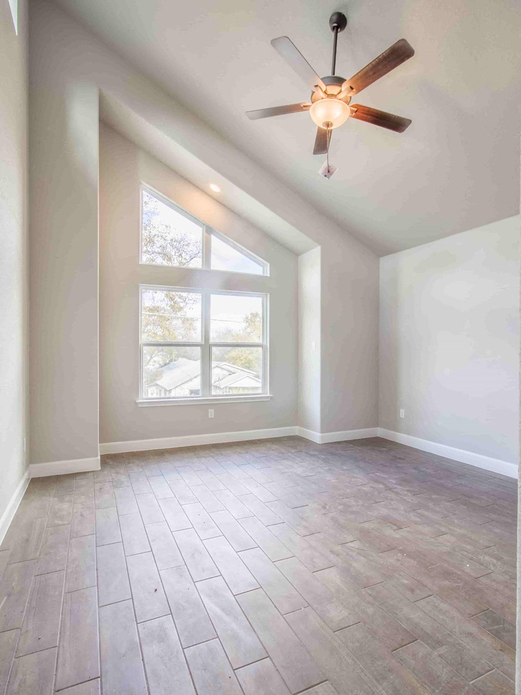 an empty living room with a large window and a ceiling fan