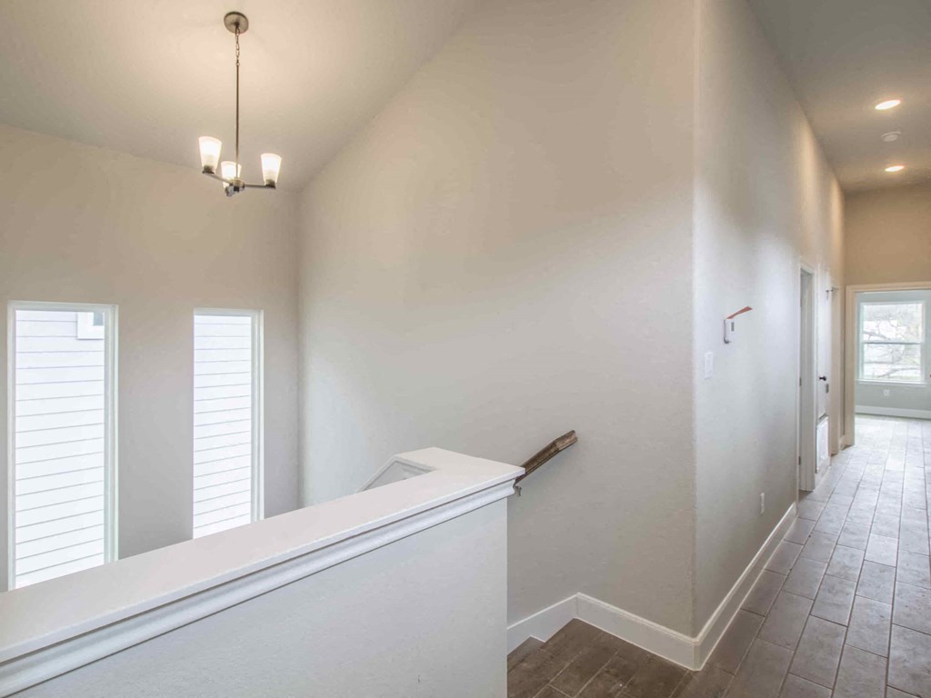 a long hallway with white walls and a white railing and a staircase