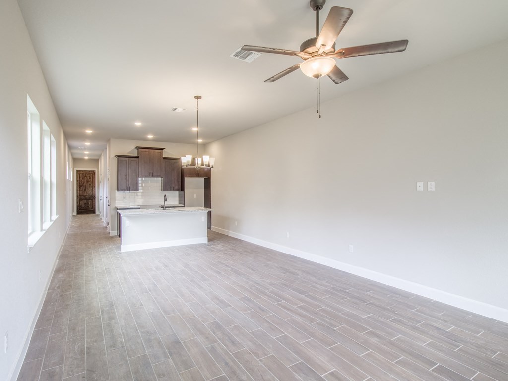 an empty living room with a ceiling fan and a kitchen