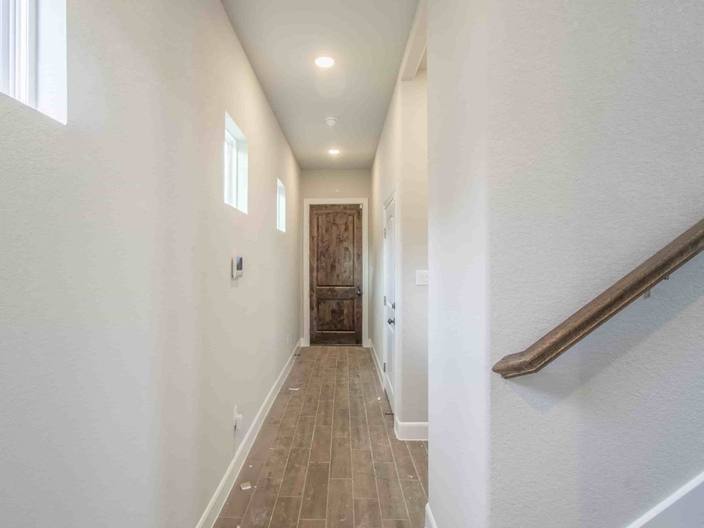 a long hallway with white walls and a wooden door and a staircase
