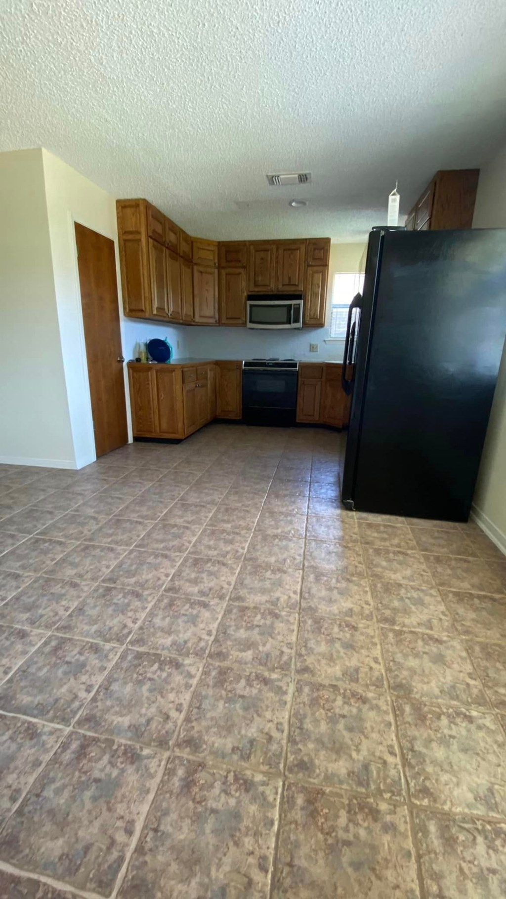 an empty kitchen with a black refrigerator and wooden cabinets