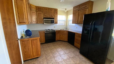 an empty kitchen with wooden cabinets and a black refrigerator