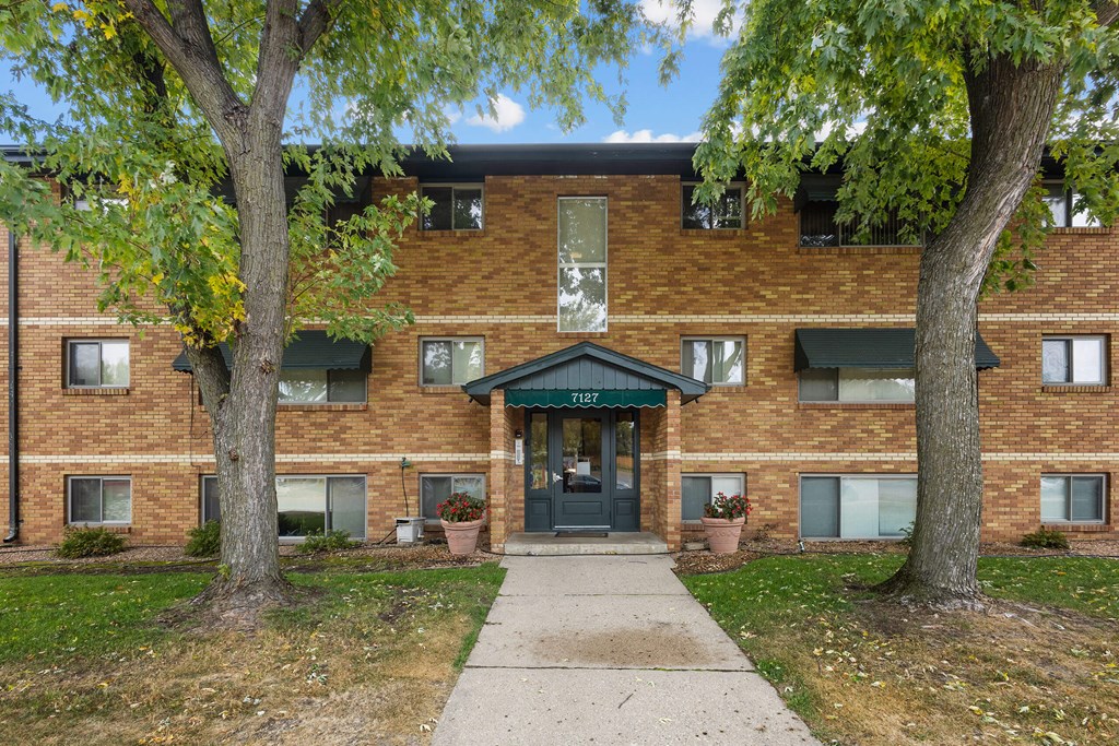A brick building with a green awning and a tree in front.