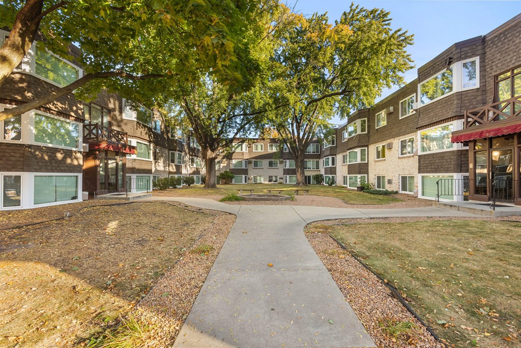 A tree-lined walkway leads to a courtyard between two buildings.
