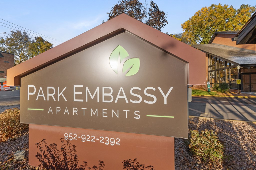 A sign for Park Embassy Apartments with a phone number on it.