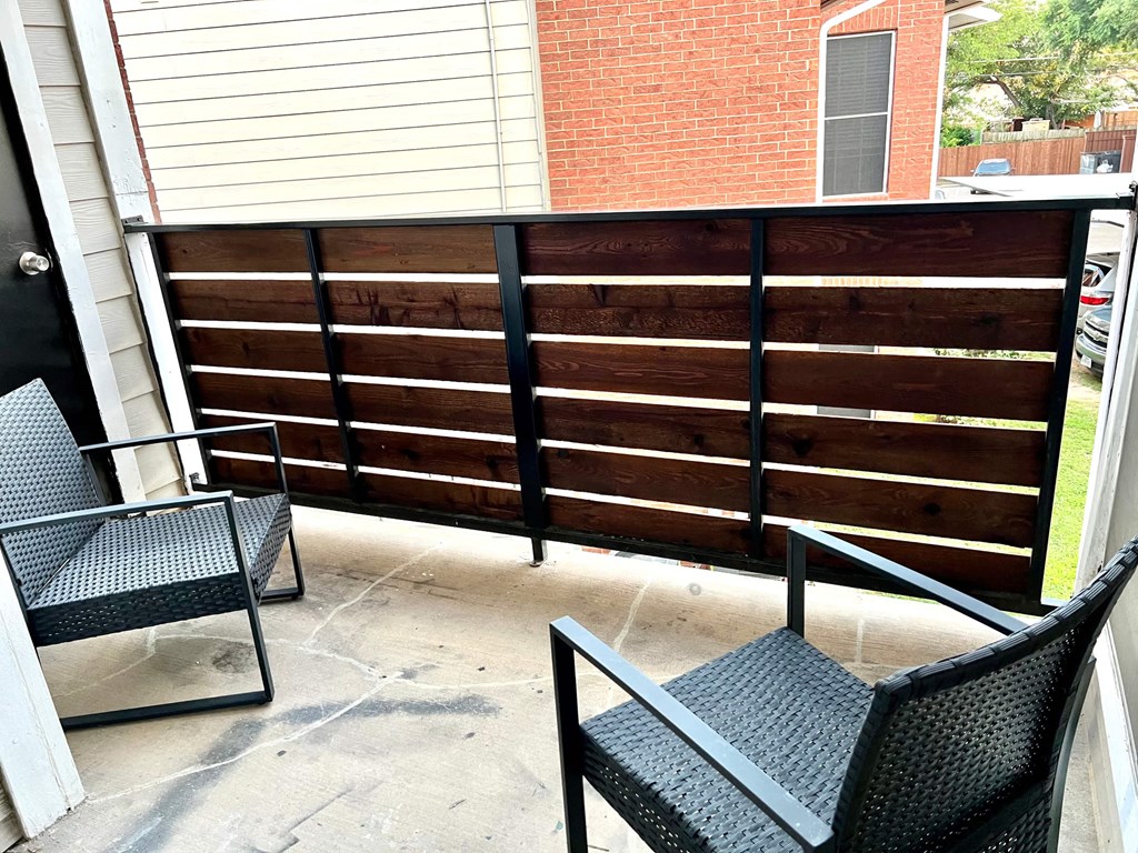 a patio with a black fence and two chairs