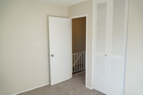 a bedroom with white closet doors and a hallway with a staircase
