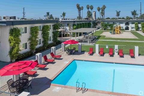 A pool with red umbrellas and chairs is surrounded by a fence.
