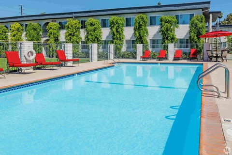 A swimming pool with red lounge chairs and a building in the background.