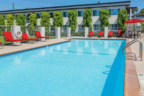 A swimming pool with red lounge chairs and a building in the background.