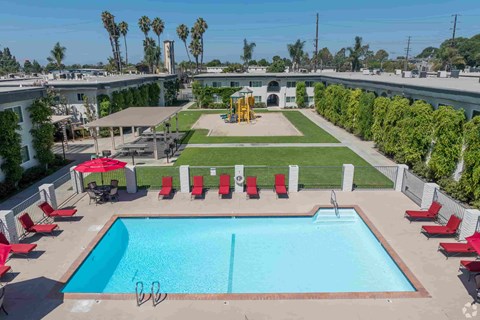 A pool with a diving board and red chairs.