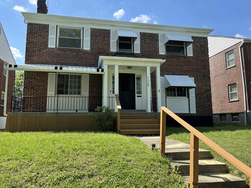 the front of a brick house with a porch and stairs