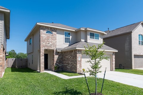 a tan and brick house with a garage and a lawn