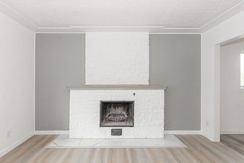 the living room has a white brick fireplace and wooden floors