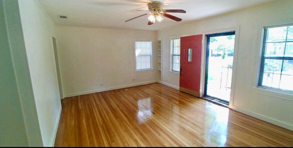 an empty living room with a red door and a ceiling fan