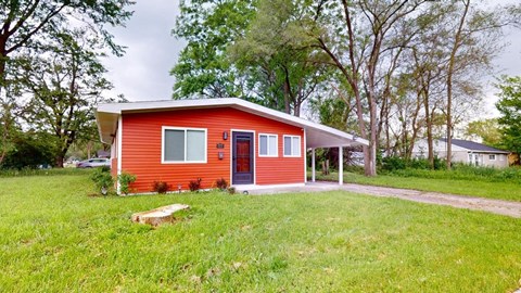 a small red house with a yard and a driveway