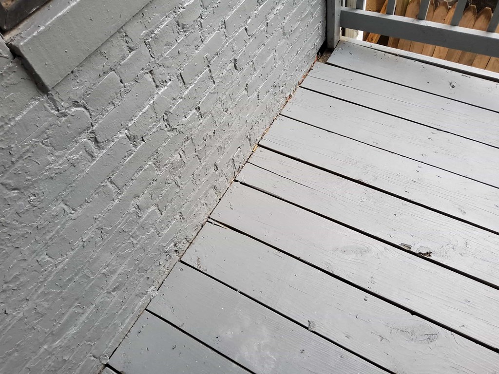 the side of a brick wall with wooden flooring next to a wooden porch
