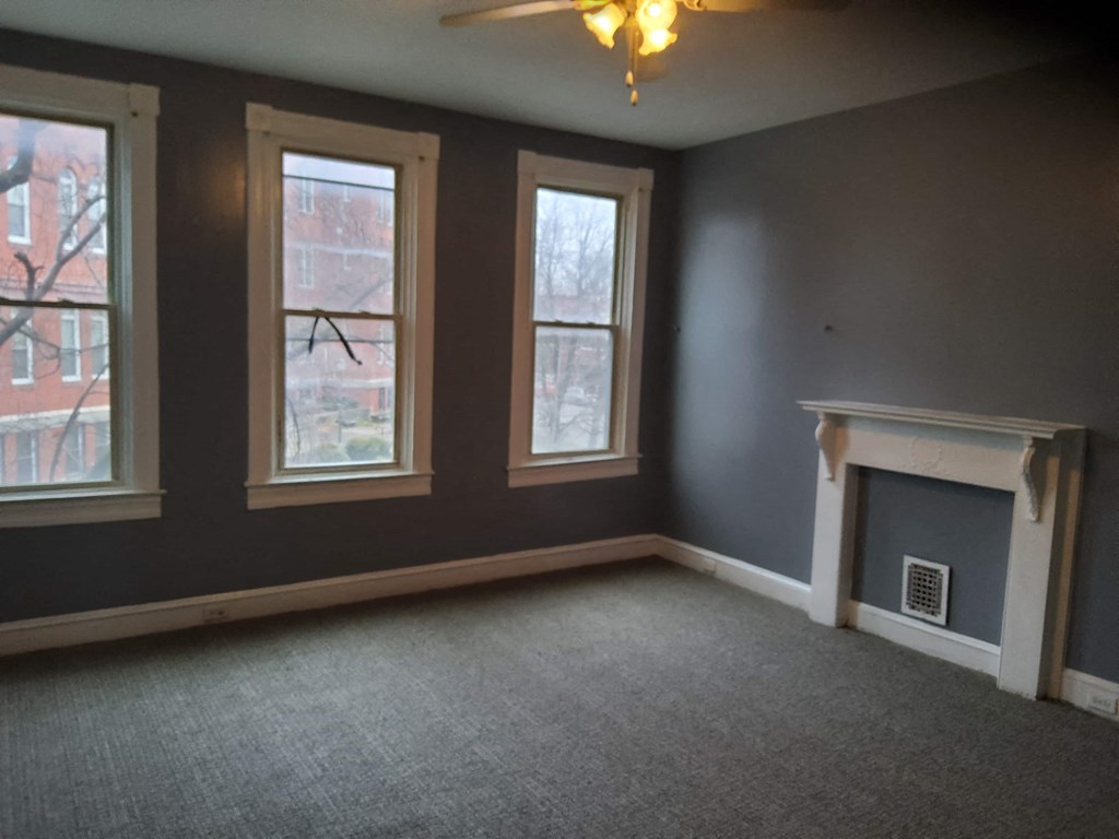 an empty living room with a fireplace and three windows