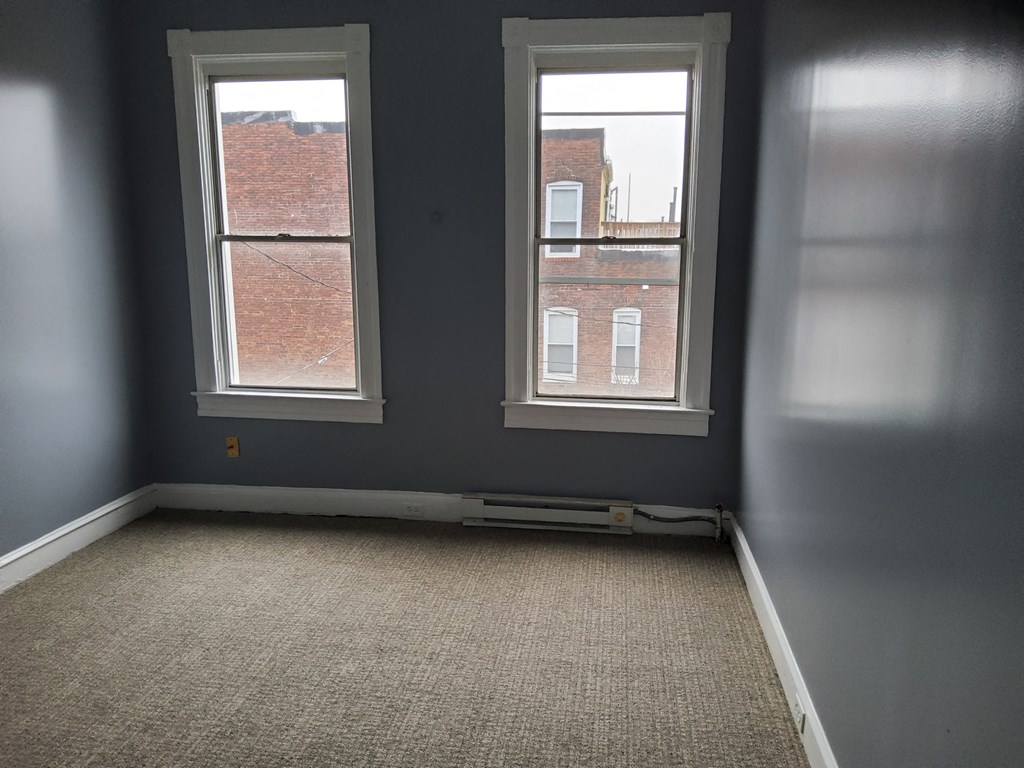 an empty room with two windows and a carpet