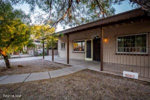 the front of a house with a sidewalk and a tree