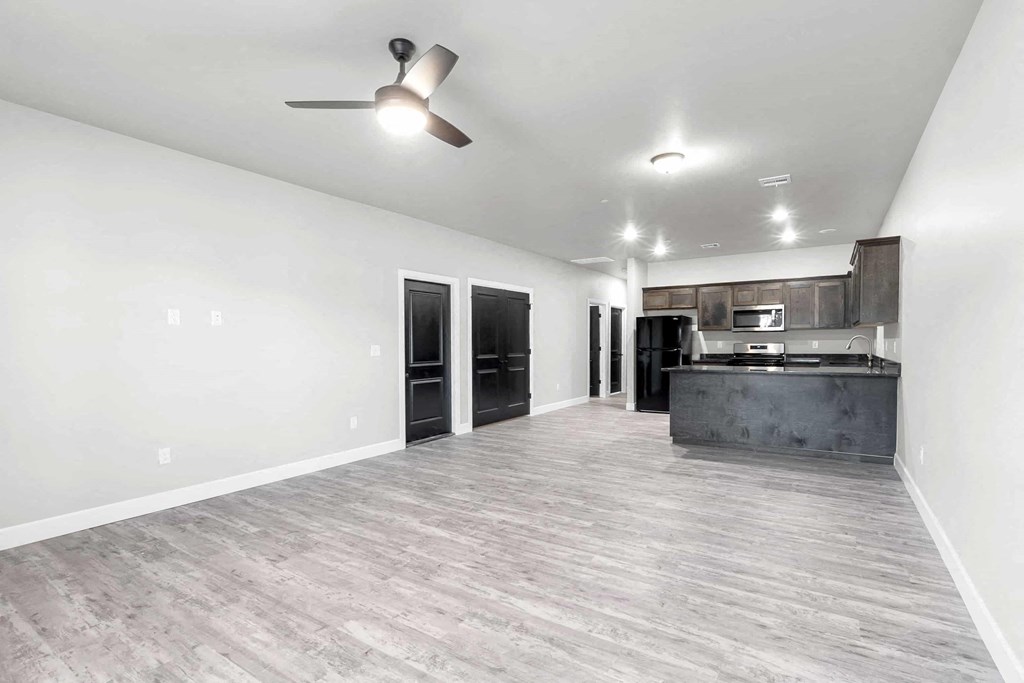 an empty living room with a kitchen and a ceiling fan