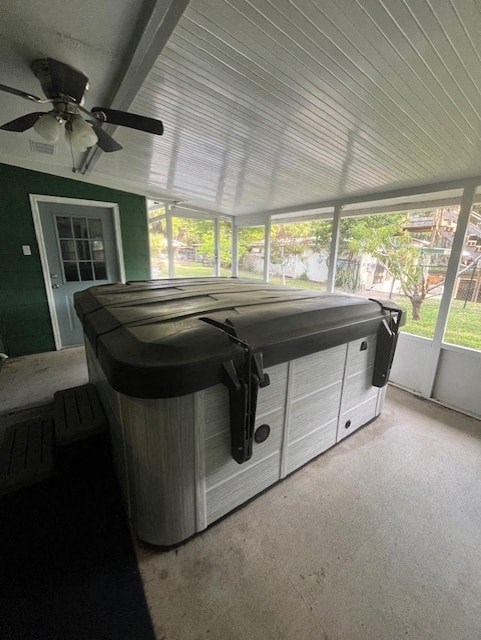 a screened in porch with a hot tub and a ceiling fan