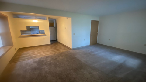 an empty living room with wood floors and a kitchen