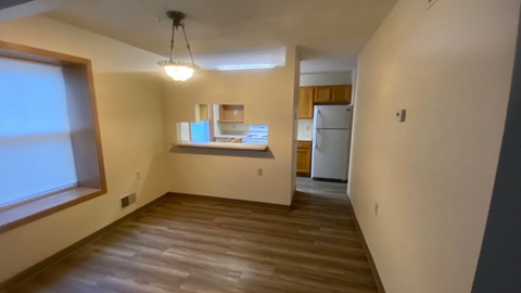 an empty living room with a kitchen and a window