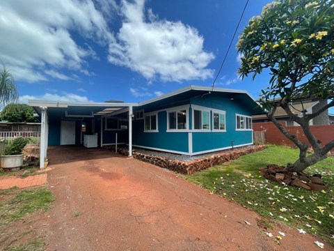 a blue house with a dirt driveway and a tree