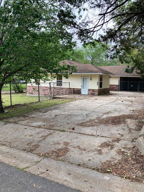a small yellow house with a driveway and a fence