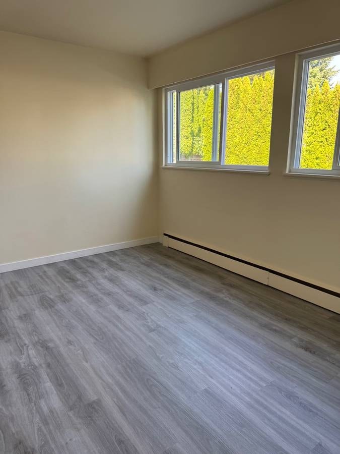 A room with grey flooring and two windows.