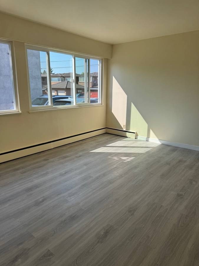 A room with light wood flooring and a window overlooking a street.