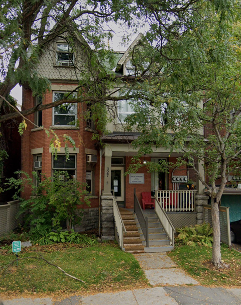 A red brick building with a porch and a tree in front.