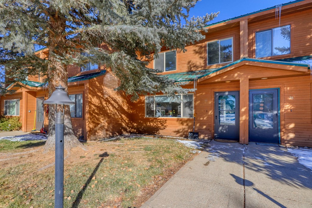 the front of a wooden house with a sidewalk and a tree